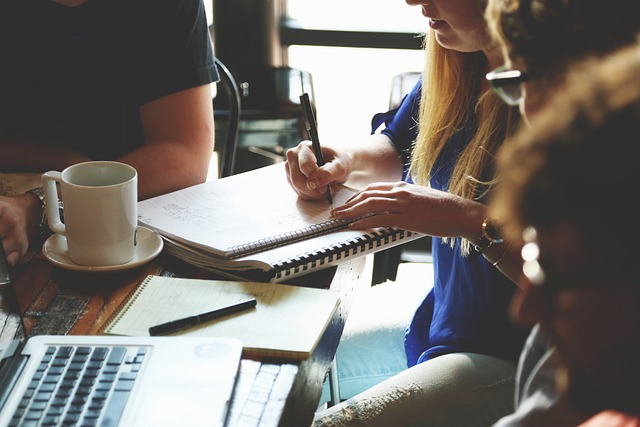 grupo de personas reunidas en una mesa con un ordenador, una libreta y un café